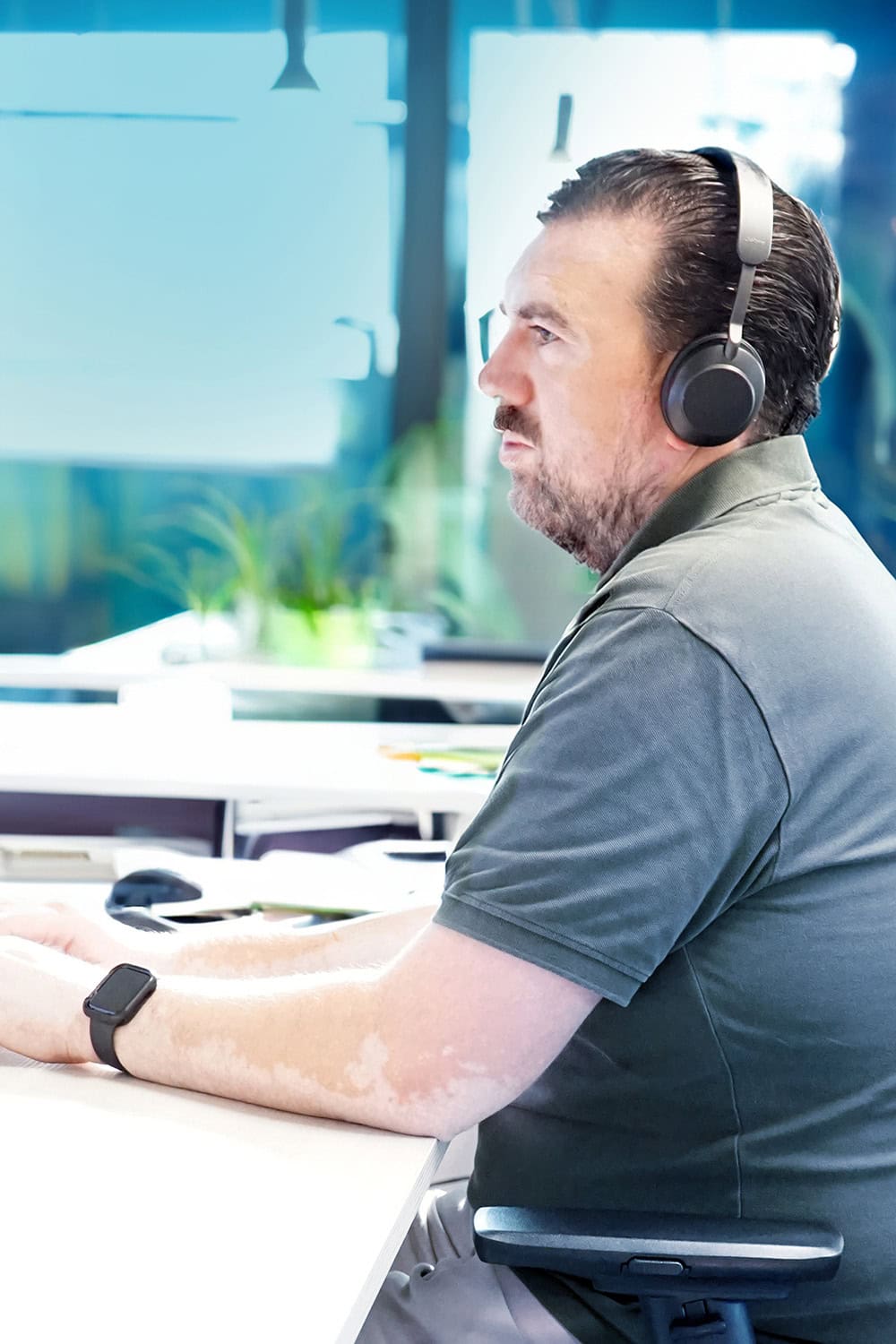 Mannelijke medewerker met koptelefoon op de serviceafdeling van Barry Emons, zittend aan een bureau op kantoor.