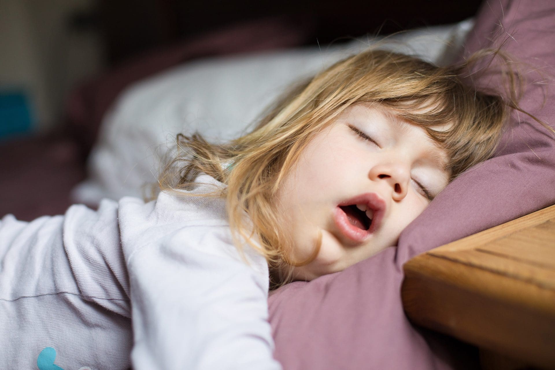 Een meisje met het down syndroom slaapt met mond open op een bed.