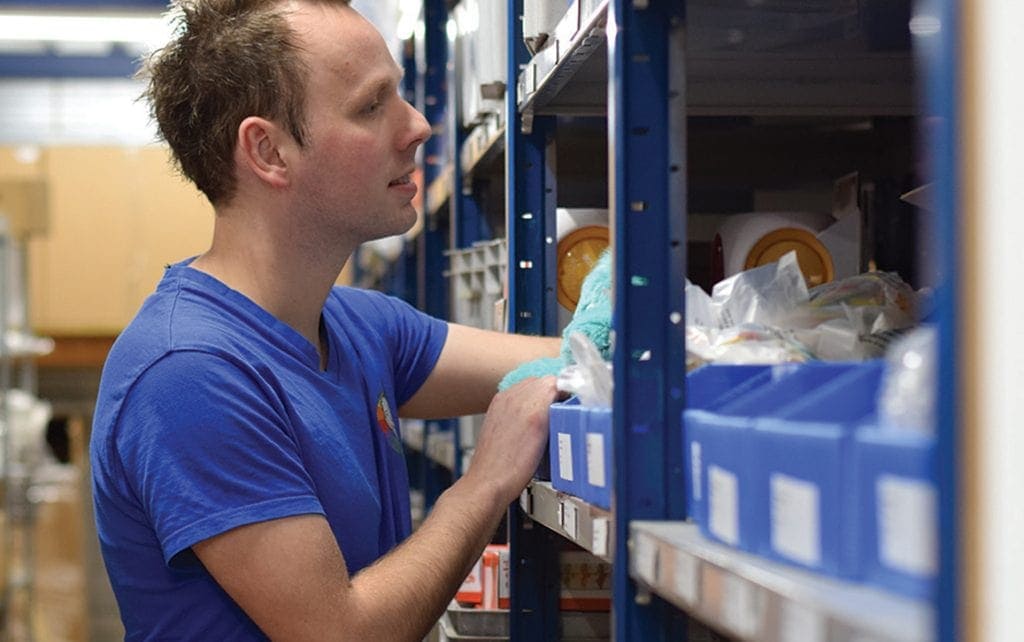 Een werknemer van Barry Emons staat naast een stelling in het magazijn en pakt iets uit de stelling.